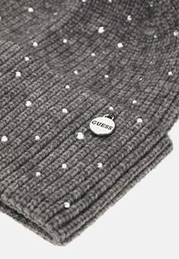 Cappello in maglia grigia a coste con strass sparsi e un piccolo tag argento con il logo "GUESS". Texture morbida e vestibilità aderente.