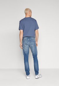 Kék rövidujjú ing, laza szabásban, világoskék skinny farmernadrággal párosítva. Fehér sportcipő szürke részletekkel. Egyszerű dizájn, laza stílus.