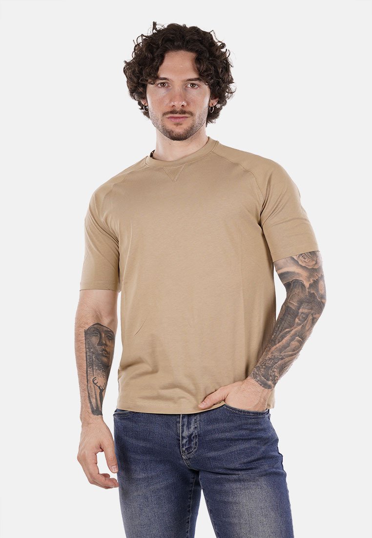 T-shirt beige a maniche corte con collo rotondo e maniche raglan. Tessuto morbido e design minimalista, abbinato a jeans blu scuro.