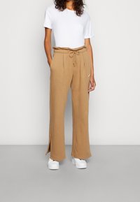 Beżowe dresy z ściągaczem w pasie i sznurkiem, posiadające boczne kieszenie i rozcięcia u dołu, połączone z gładką białą koszulką.