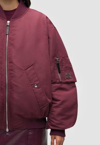 Bourgognefärgad bomberjacka med ribbade muddar och fåll, blixtlåsförslutning framtill, oversized passform, med blixtlåsförsedd ficka och logobroderi på ärmen.