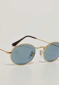 Gafas de sol redondas con montura de metal dorado, lentes de tono azul y acentos de carey en las varillas. Con almohadillas nasales para mayor comodidad.