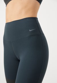 Legginsy o wysokim stanie w ciemnoniebieskim kolorze z gładkiej tkaniny. Wyróżniają się delikatnym, szarym logo Nike na pasku.