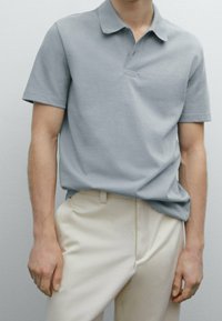 Lys grå polo shirt i blødt stof med klassisk krave og korte ærmer, parret med cremefarvede bukser. Simpelt design og pasform.