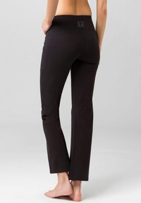 Black yoga pants with a wide waistband, tapered legs, and side pockets. Smooth texture, casual fit, and logo detail on the waistband.
