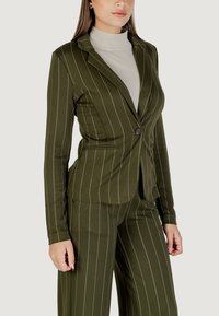 Blazer vert olive avec des fines rayures, fermeture à un bouton, deux poches latérales, coupe ajustée et texture lisse, associé à un léger col roulé.