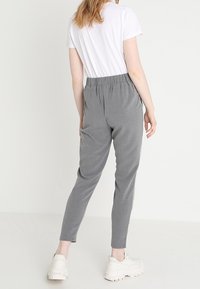 Grijze, taps toelopende joggingbroeken met een elastische tailleband, gecombineerd met een wit T-shirt, gezien van achteren, minimale details, gladde textuur.