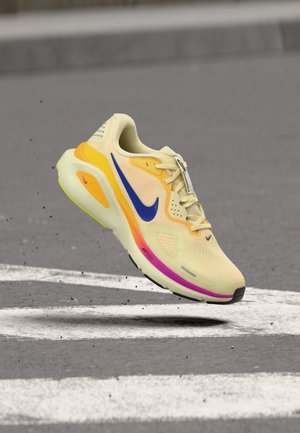 Light yellow Nike running shoe with blue swoosh, orange and pink sole accents, mid-air over a gray asphalt surface with white markings.