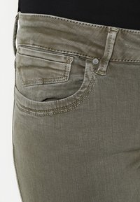 Tmavě olivové džíny vyrobené z denimu, s klasickým pětipocket designem, viditelným prošíváním a mírně vybledlou texturou.