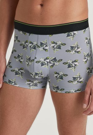 Herren Boxershorts mit grauem Grund, ausgestattet mit einem wiederholten Muster von Kuhköpfen in Grün und Schwarz. Hergestellt aus weichem, dehnbarem Material mit einem schwarzen Bund.