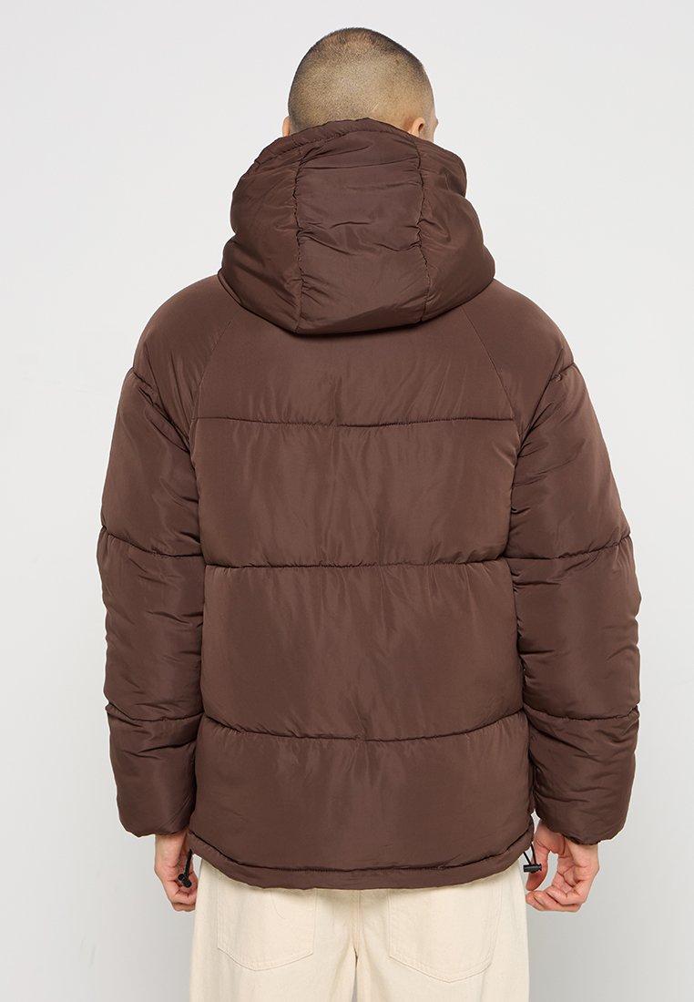 Braune gepolsterte Jacke mit Kapuze, die ein gestepptes Design und elastische Bündchen aufweist. Der Stoff wirkt glatt und leicht.