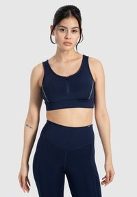 Marineblauwe sportbeha met een rits aan de voorkant, brede banden en reflecterende accenten. Heeft een aansluitend ontwerp en een zachte textuur, in combinatie met hooggesneden legging.