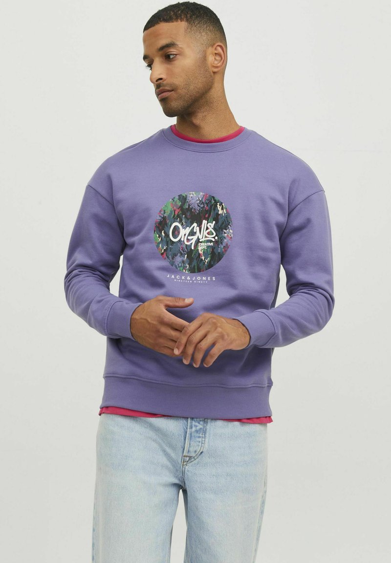 Sudadera morada hecha de suave algodón, con un logo gráfico multicolor circular en la parte frontal. Diseño de cuello redondo con puños acanalados.