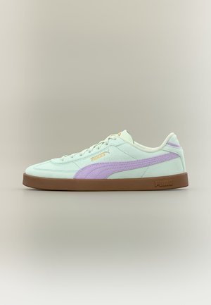 Jasnozielony but sportowy Puma z lawendowym paskiem po boku i brązową podeszwą, pokazany z boku na neutralnym tle.