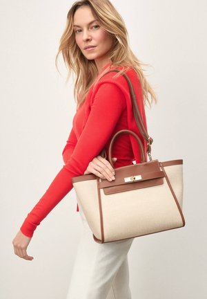 Sac à main en toile beige avec des accents en cuir marron et une forme structurée ; dispose d'une poignée supérieure et d'une bandoulière détachable.
