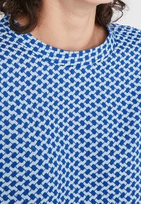 Maglione a maglia blu e bianco con scollatura rotonda, caratterizzato da un design geometrico e una texture morbida.