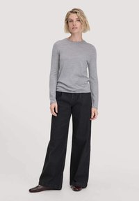Grijze lange mouwen aansluitend top gecombineerd met hoge taille wijde zwarte spijkerbroek. De outfit heeft een gladde textuur en een minimalistisch ontwerp.