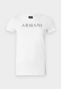 T-shirt branca de algodão com letras metálicas prateadas "ARMANI" na frente. Mangas curtas e gola redonda.