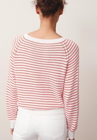 Pull rayé rouge et blanc avec un col rond, des poignets côtelés et un design légèrement court. Matière tricotée douce avec des détails de texture subtils.