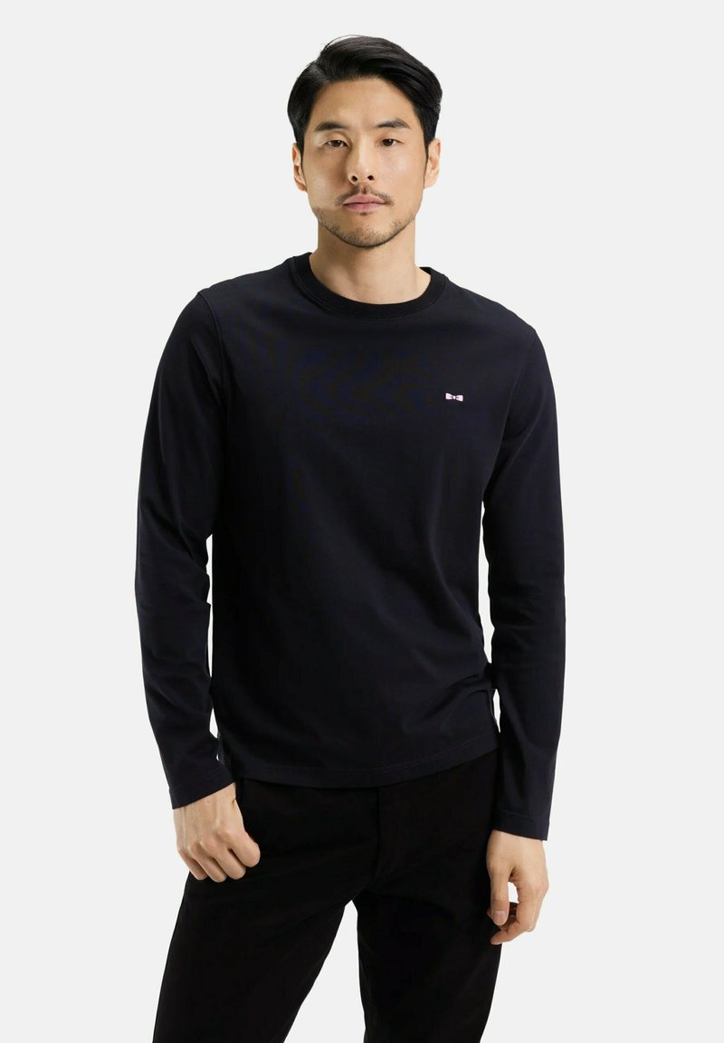 T-shirt noir à manches longues en tissu doux, avec un col rond et un petit logo sur la poitrine. Design simple sans motifs supplémentaires.