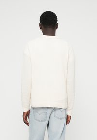Hvid tekstureret sweater med krave, lange ærmer og ribbede manchetter, parret med lyseblå denimjeans.