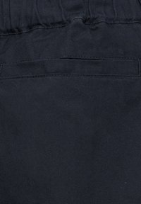 Close-up van donkerblauwe stof met elastische tailleband en horizontale stikseldetail van een paspelzak.