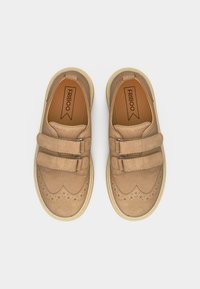 Παιδικά παπούτσια από ταμπά σουέτ με λεπτομέρειες μπρόγκου, διπλές λουρίδες με βέλκρο και λαστιχένιες σόλες σε κρεμ χρώμα, τακτοποιημένα απέναντι σε λευκό φόντο.