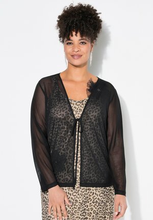 Cárdigan negro transparente con mangas largas, cierre frontal con lazo y detalles florales, superpuesto sobre un vestido de estampado de leopardo.