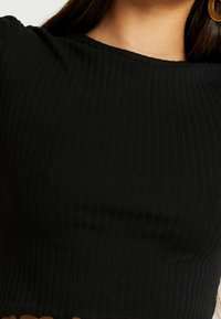 Schwarzes geripptes Cropped-Top mit Rundhalsausschnitt und enganliegendem Design. Glatte Textur mit horizontalen Rillen, die die Dehnbarkeit des Stoffes betont.