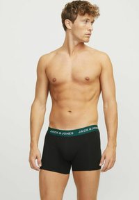 Boxer shorts negros con una cinturilla verde que presenta el texto "JACK & JONES". La cinturilla es elástica y la tela parece suave y ajustada.