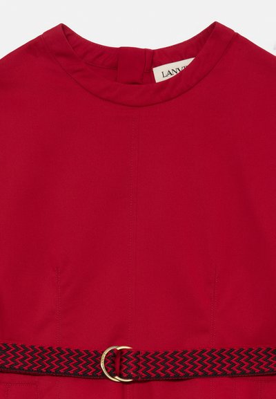 Vestido vermelho com decote redondo e costuras em forma de pinça, apresentando um cinto zig-zag em preto e vermelho com fivela circular dourada.