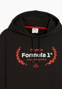 Sort hoodie med en rød indvendig foring, der har hvid og rød tekst: "75 år med Formel 1 - af fart og adrenalin. ET. 1950."