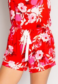 Röd blommig jumpsuit med rosa och vita blommor, elastisk midja och en vit dragsko. Lätt, slätt tyg med sidofickor.