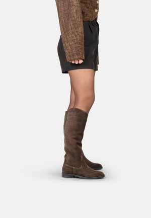 Stivali alti fino al ginocchio in suede marrone con suola piatta e punta arrotondata, caratterizzati da un design semplice e una texture liscia, posizionati su uno sfondo neutro.