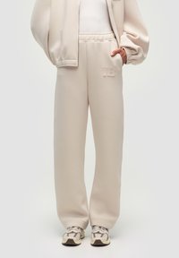 Helle beige Sweatpants aus weichem Stoff, mit einem lässigen Schnitt, elastischem Bund und einem dezenten, aufgenähten "WB"-Logo auf der Vorderseite.