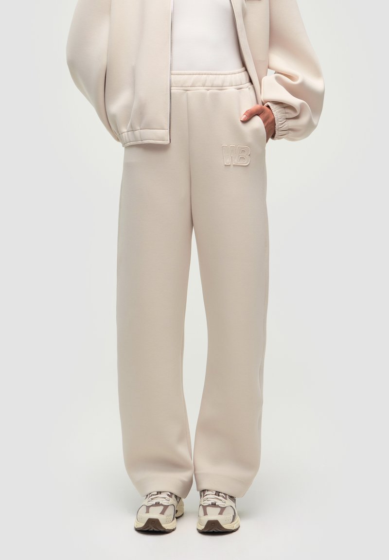 Helle beige Sweatpants aus weichem Stoff, mit einem lässigen Schnitt, elastischem Bund und einem dezenten, aufgenähten "WB"-Logo auf der Vorderseite.