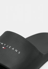 Sorte sandaler med teksturert overflate, som har en hvit logo "MYJEANS" og en rød og hvit aksent under teksten.