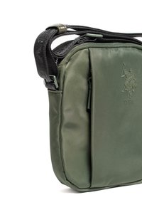 Kompaktowa oliwkowozielona torebka na ramię z czarnym regulowanym paskiem, przednią kieszenią na zamek oraz wytłoczonym logo USPA z dwoma graczami polo.