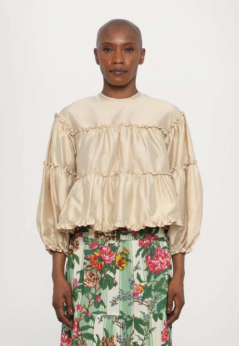 Top in satin beige con volants e maniche lunghe a sbuffo. Abbinato a una gonna colorata con stampa floreale e righe verdi.