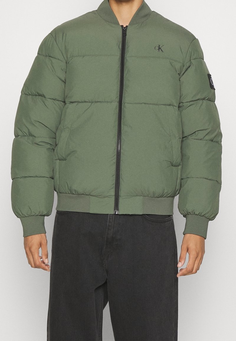 Groene gewatteerde jas met een ritssluiting aan de voorkant, geribde manchetten en zoom. Heeft een logo op de borst en een zijzak aan de linkerkant.