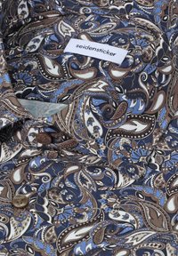 Chemise à motif cachemire bleu, marron et blanc avec des boutons marron et une étiquette visible portant la mention "seidensticker" sur le col.