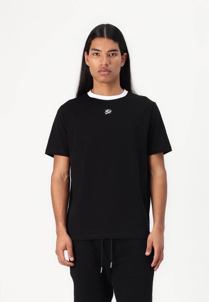 Svart t-shirt med vit ribbad krage och broderad logotyp på bröstet. Kort ärm, avslappnad passform, tillverkad av mjukt bomullsmaterial.