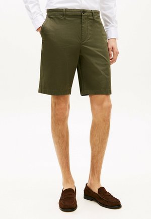 Pantalones cortos verde olivo con frente plano, trabillas para cinturón y bolsillos laterales; tejido de mezcla de algodón, a la altura de la rodilla, combinados con mocasines marrones.