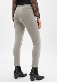 Graue Skinny-Jeans mit einer glatten Textur, mittelhoher Taille, Gesäßtaschen und kombiniert mit schwarzen Stiefeletten und einem Leopardenmuster-Oberteil.