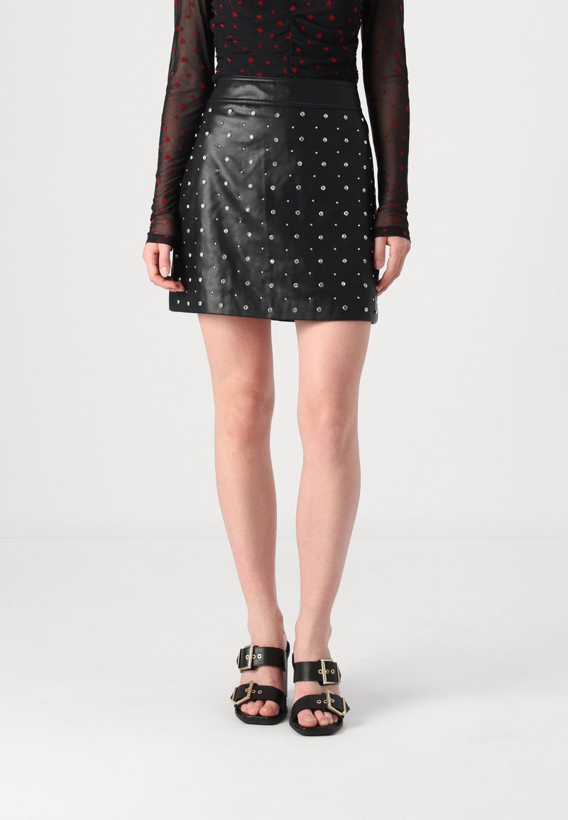Svart skinn mini skjørt med sølvnagler i prikkmønster, med en glatt tekstur og høy midje. Svart sandaler med spenner.