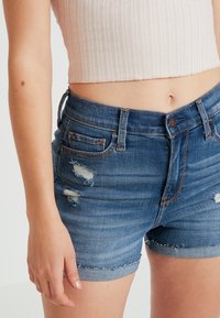 Denim shorts in dark wash with distressed detailing and frayed hem. Features visible stitching and side pockets, fitted at the waist.