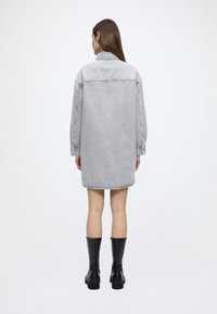 Grå denimskjortekjole med lange ærmer, krave og sidelommer, der ender over knæet. Parret med knæhøje sorte støvler.