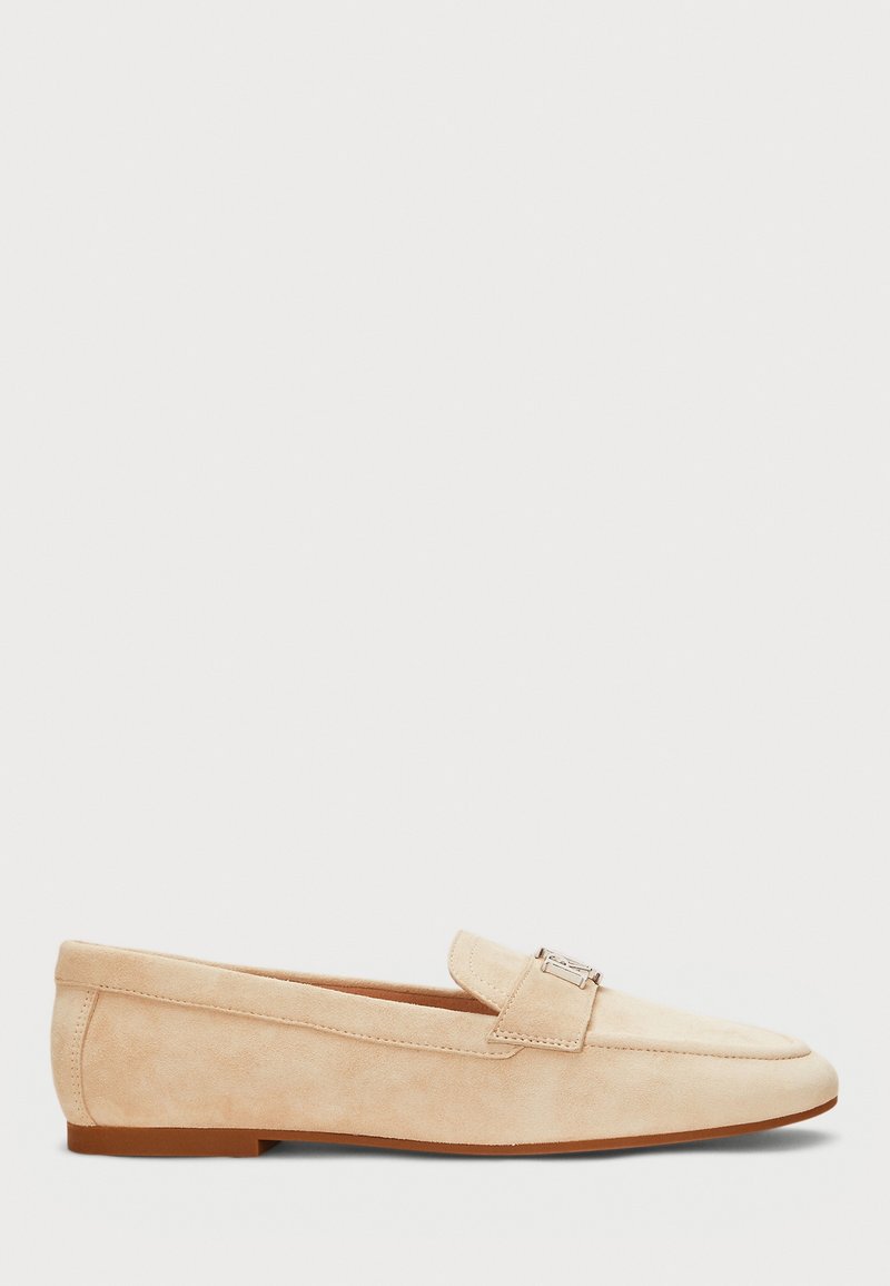 Mocassin en daim beige avec un petit talon et une boucle argentée sur le dessus, vu de côté sur fond blanc.