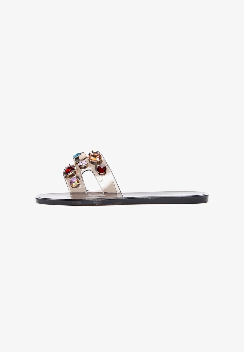 Transparent slide sandal with a flat black sole, featuring multi-colored gem accents on the upper strap in various shapes and sizes.