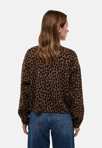 Pull marron à imprimé léopard noir, coupe ample, manches longues et texture côtelée. Porte avec un jean taille haute bleu clair.